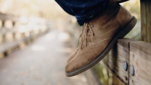Close-up van bruin suède schoenen aan voeten op een houten hek, perfect voorbeeld voor suède schoonmaken