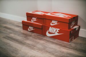 Vier rode Nike schoenendozen gestapeld op een houten vloer tegen een witte muur. 