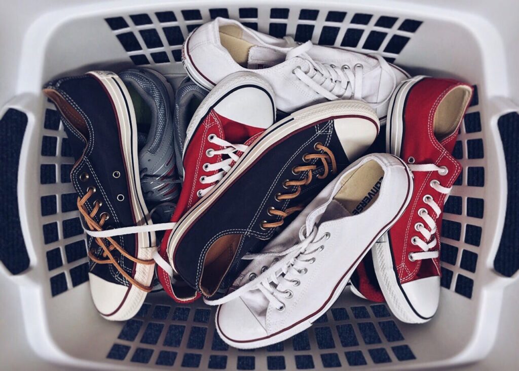 Canvas sneakers in verschillende kleuren liggen in een witte wasmand, klaar om gewassen te worden.